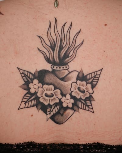 Cœur sacré entouré de fleurs tatoué en noir et gris dans le dos