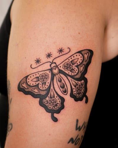 Papillon aux ailes fleuries tatoué en noir et gris sur un bras