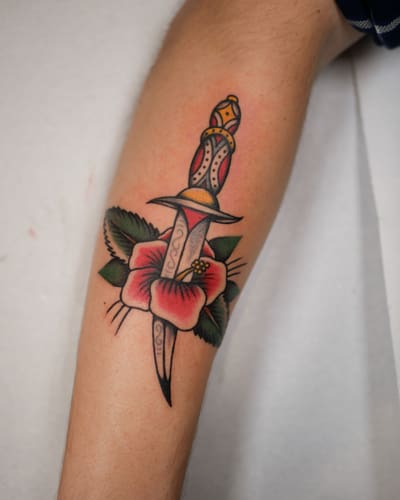 Dague traversant une fleur rouge tatouée en couleur sur un avant-bras