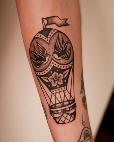 Montgolfière ornée de deux hirondelles tatouée en noir et gris